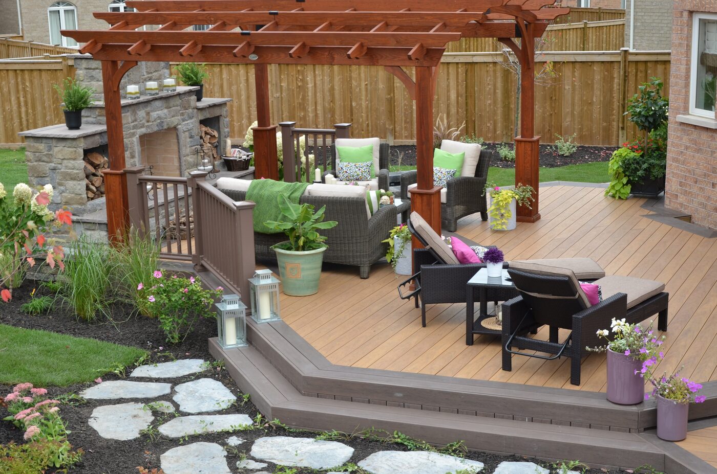 Composite backyard deck with pergola, fireplace, seating, and planted edges